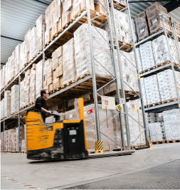 A warehouse with tall shelves filled with boxes. A forklift is being operated by a person.